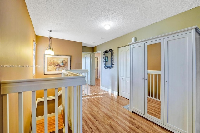 hall featuring light wood finished floors, baseboards, a textured ceiling, and an upstairs landing