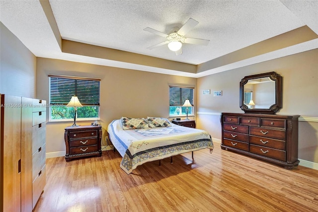 bedroom with a ceiling fan, baseboards, a textured ceiling, and light wood finished floors