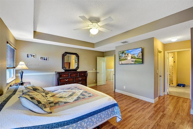 bedroom with a raised ceiling, visible vents, light wood-style flooring, a textured ceiling, and baseboards