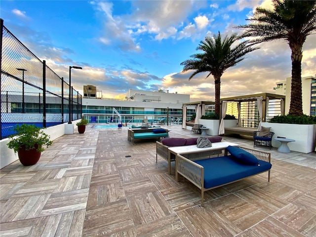 patio terrace at dusk with a tennis court, fence, and outdoor lounge area