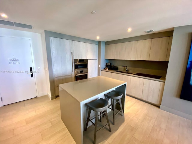 kitchen with visible vents, a kitchen island, light countertops, a kitchen bar, and a sink