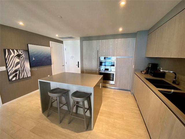 kitchen with a kitchen island, a breakfast bar area, light countertops, double oven, and a sink