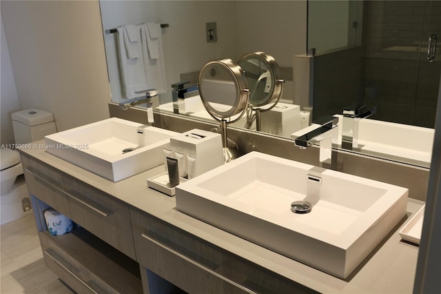 bathroom with double vanity, a stall shower, toilet, and a sink