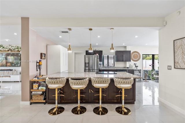 kitchen featuring a breakfast bar, stainless steel refrigerator with ice dispenser, light tile patterned floors, hanging light fixtures, and light stone countertops