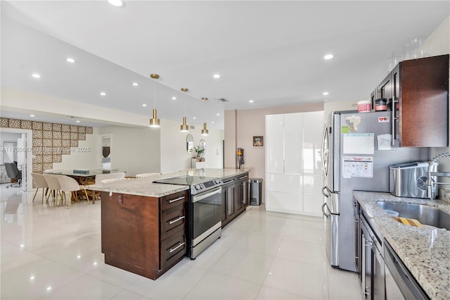 kitchen featuring appliances with stainless steel finishes, a sink, light stone countertops, and pendant lighting