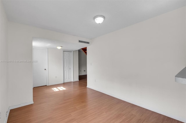 spare room featuring a textured ceiling, light wood finished floors, visible vents, and baseboards