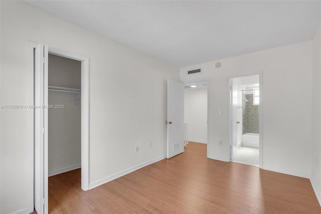 unfurnished bedroom with baseboards, visible vents, light wood-style flooring, a walk in closet, and a closet