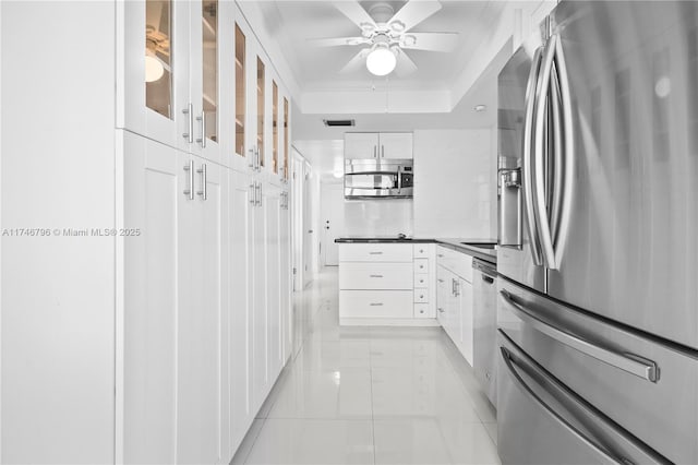 kitchen with dark countertops, a raised ceiling, appliances with stainless steel finishes, glass insert cabinets, and white cabinetry