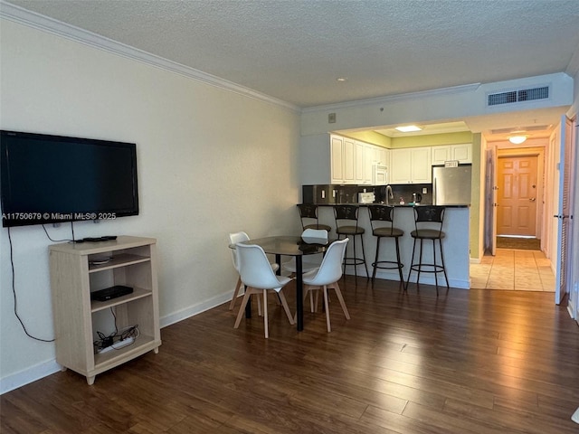 dining area featuring baseboards, visible vents, dark wood-style floors, ornamental molding, and a textured ceiling