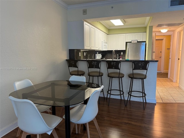 dining space featuring baseboards, wood finished floors, visible vents, and crown molding