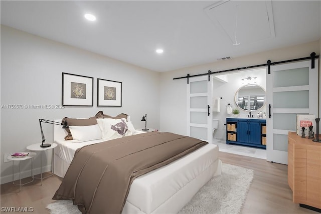 bedroom featuring a barn door, attic access, visible vents, light wood-type flooring, and a sink