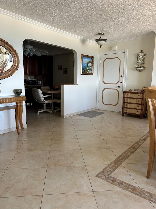 foyer entrance featuring light tile patterned floors, baseboards, arched walkways, a textured ceiling, and crown molding