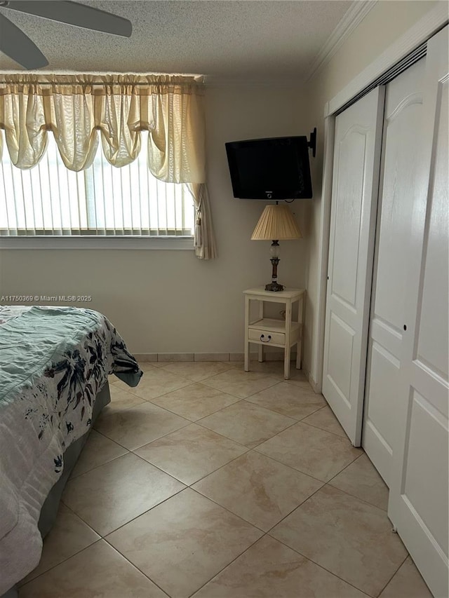 bedroom featuring a closet, ornamental molding, a textured ceiling, tile patterned flooring, and baseboards