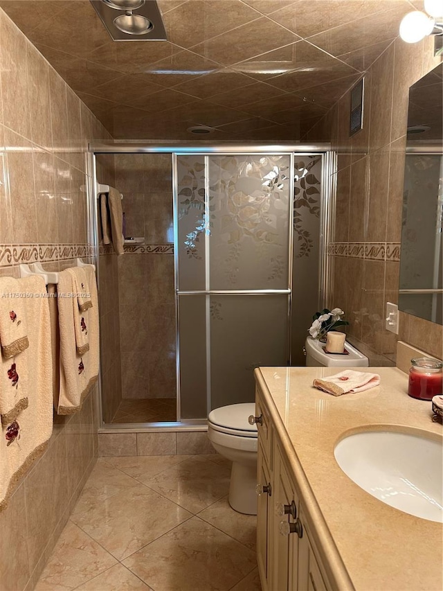 bathroom with toilet, tile patterned flooring, vanity, a shower stall, and tile walls