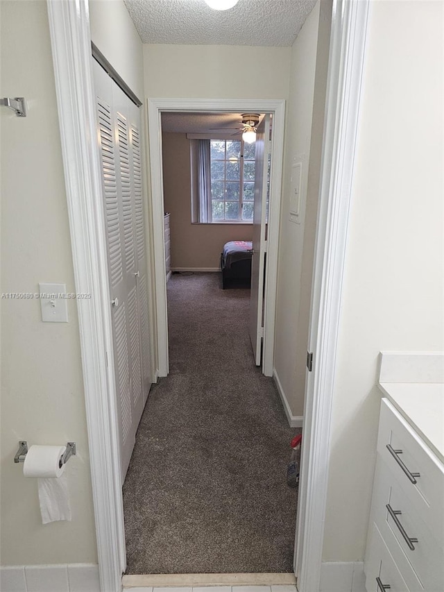 hallway featuring carpet floors, a textured ceiling, and baseboards