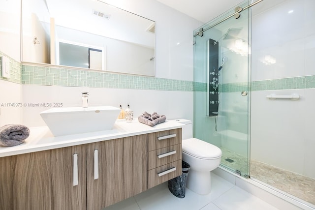 bathroom with a stall shower, visible vents, toilet, vanity, and tile walls