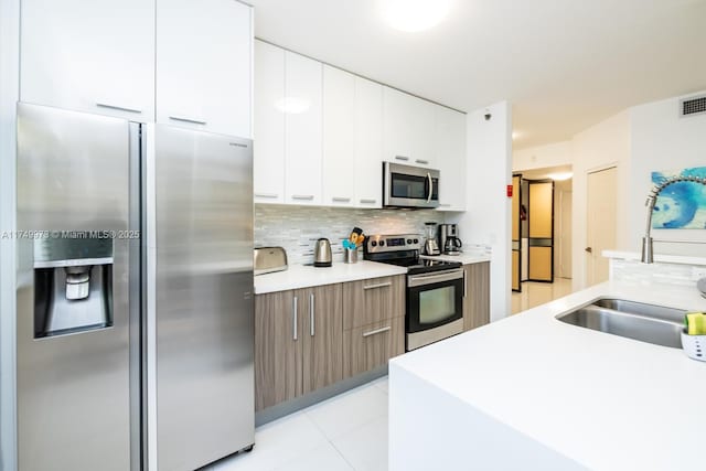 kitchen featuring stainless steel appliances, light countertops, white cabinets, a sink, and modern cabinets