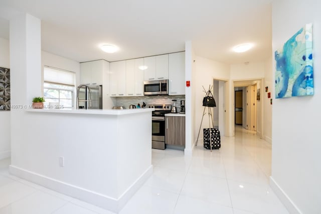 kitchen featuring appliances with stainless steel finishes, a peninsula, light countertops, white cabinetry, and backsplash