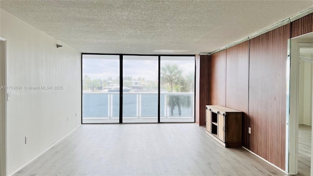 spare room with floor to ceiling windows, a water view, light wood finished floors, and a textured ceiling