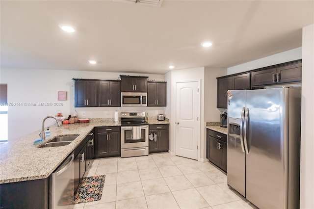 kitchen featuring stainless steel appliances, a sink, dark brown cabinetry, light stone countertops, and a peninsula