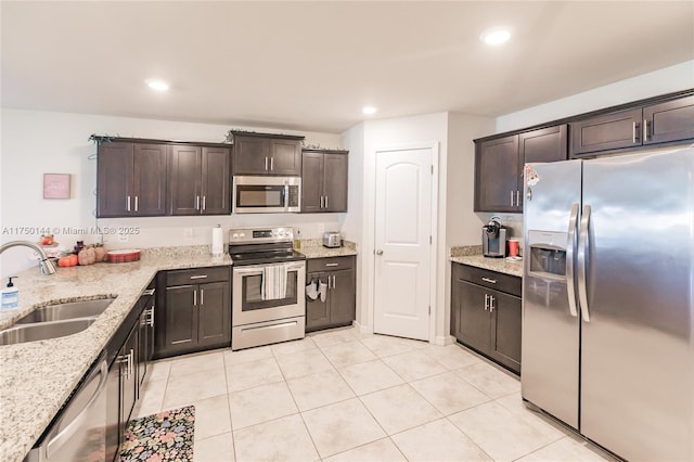 kitchen featuring dark brown cabinetry, light stone countertops, appliances with stainless steel finishes, and a sink