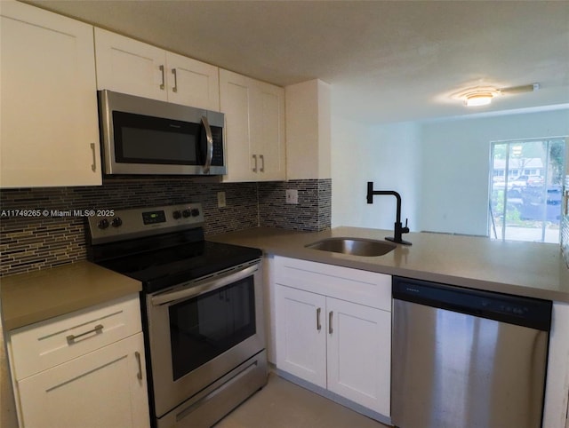 kitchen with stainless steel appliances, tasteful backsplash, a sink, and white cabinetry