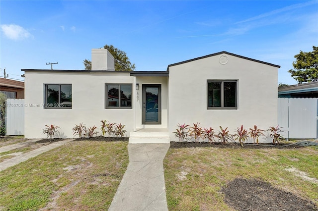 view of front of house with fence, a chimney, a front lawn, and stucco siding