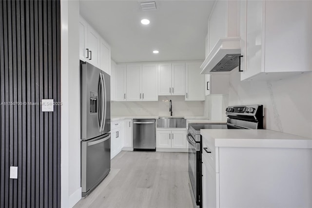 kitchen featuring light wood finished floors, appliances with stainless steel finishes, light countertops, white cabinetry, and a sink