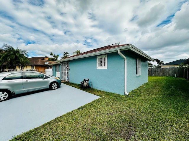 view of property exterior featuring fence, a lawn, and stucco siding