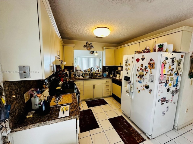 kitchen featuring light tile patterned floors, white refrigerator with ice dispenser, dark countertops, a textured ceiling, and a sink