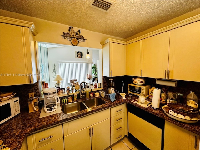 kitchen featuring visible vents, white microwave, a sink, a textured ceiling, and dark stone countertops