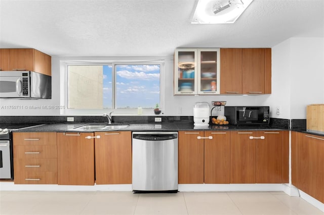 kitchen featuring glass insert cabinets, appliances with stainless steel finishes, brown cabinets, and a sink