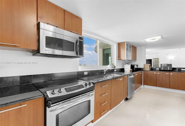 kitchen featuring dark stone counters, stainless steel appliances, brown cabinetry, and a sink