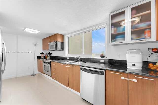 kitchen featuring glass insert cabinets, brown cabinets, stainless steel appliances, a textured ceiling, and a sink