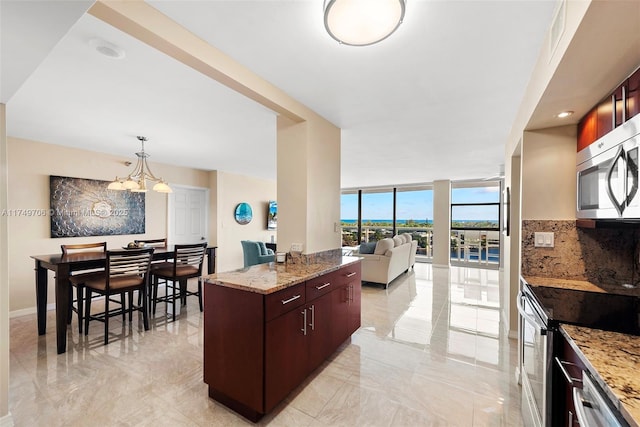 kitchen featuring marble finish floor, hanging light fixtures, appliances with stainless steel finishes, open floor plan, and light stone countertops