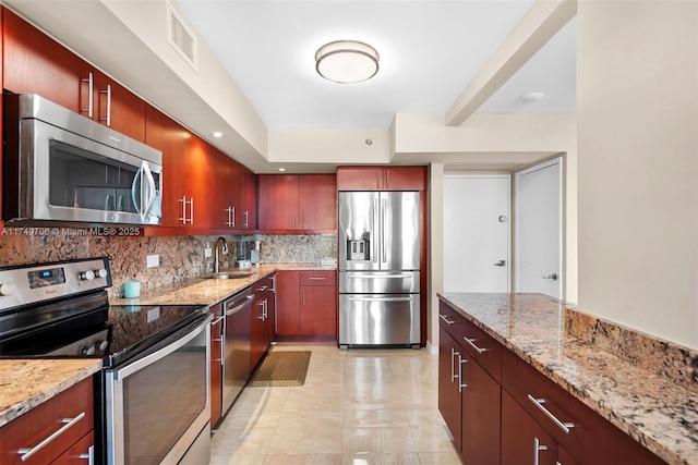 kitchen featuring reddish brown cabinets, appliances with stainless steel finishes, light stone counters, and decorative backsplash