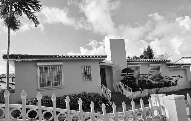 view of front facade featuring a tiled roof, a fenced front yard, an attached garage, and stucco siding