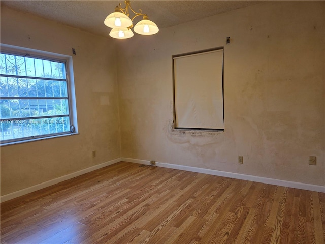 empty room with baseboards, wood finished floors, and a notable chandelier