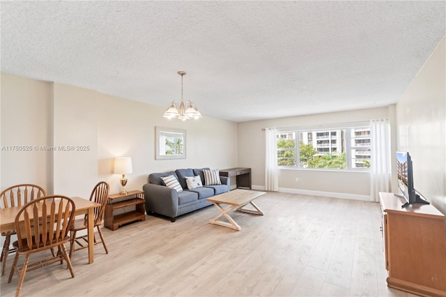 living room with baseboards, a notable chandelier, a textured ceiling, and light wood finished floors