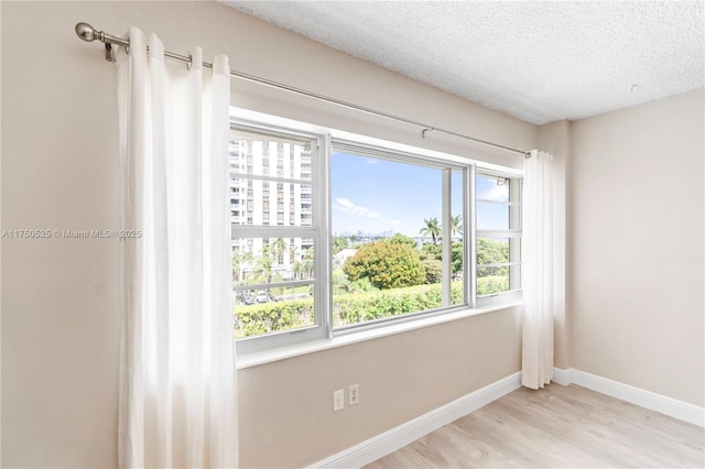 unfurnished room with a textured ceiling, light wood-style floors, and baseboards