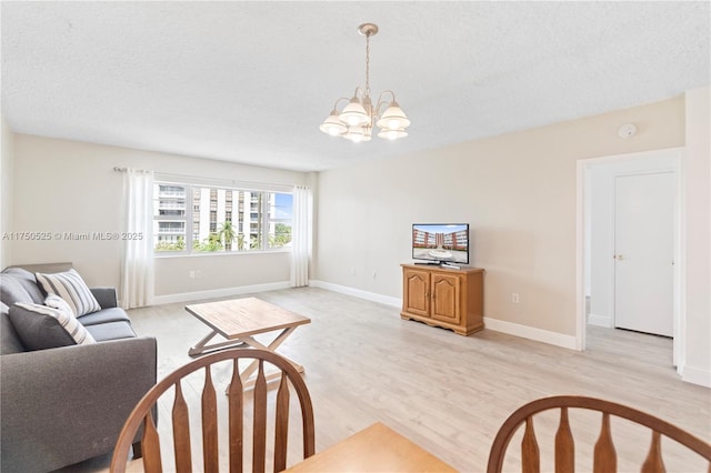 living room featuring an inviting chandelier, light wood-style flooring, baseboards, and a textured ceiling