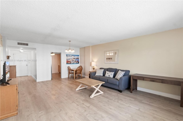 living area featuring baseboards, visible vents, a textured ceiling, light wood-style floors, and a chandelier