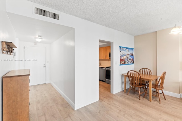 dining room with a textured ceiling, light wood-style flooring, visible vents, and baseboards