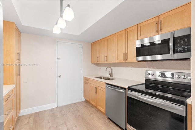 kitchen featuring appliances with stainless steel finishes, decorative light fixtures, light countertops, light brown cabinetry, and a sink