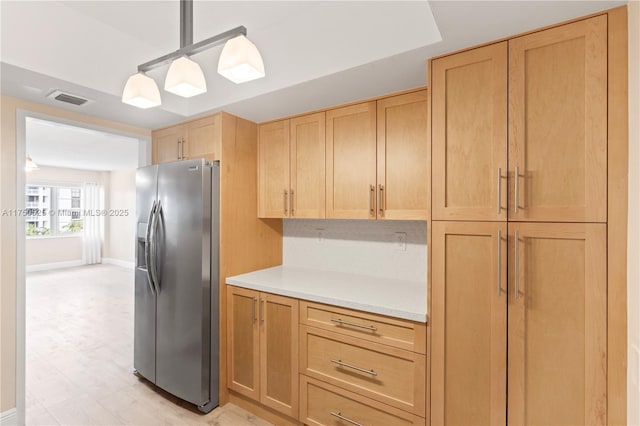 kitchen with light countertops, hanging light fixtures, visible vents, light brown cabinets, and stainless steel fridge