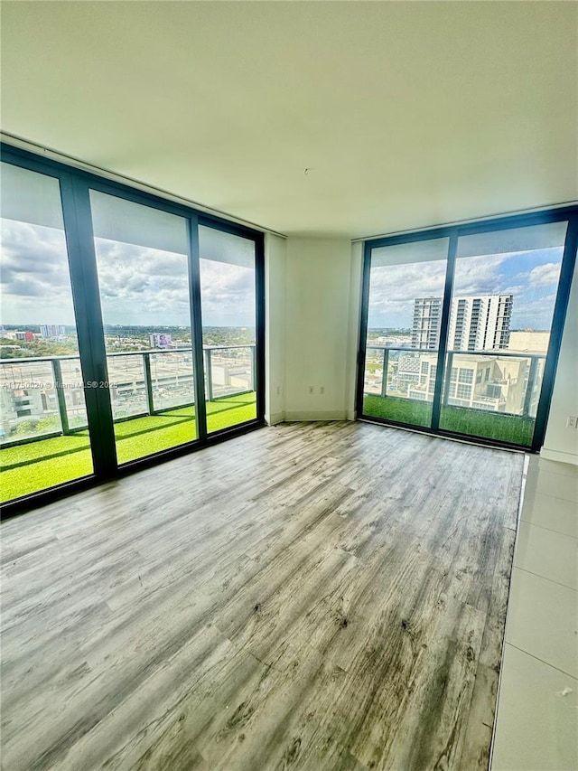 unfurnished room with a view of city, floor to ceiling windows, light wood-style flooring, and baseboards