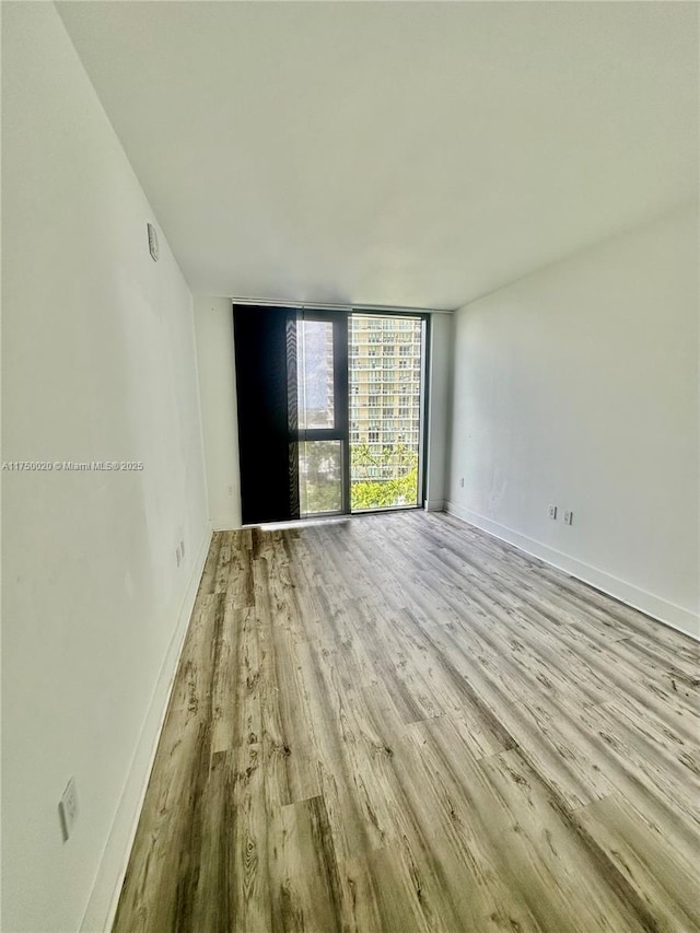 spare room with light wood finished floors, baseboards, and floor to ceiling windows