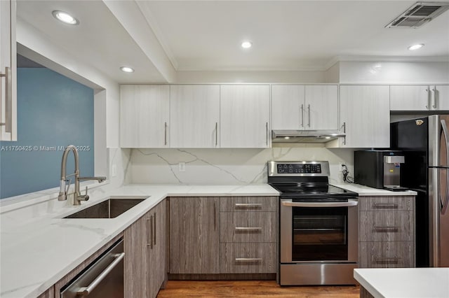 kitchen with under cabinet range hood, stainless steel appliances, a sink, visible vents, and modern cabinets