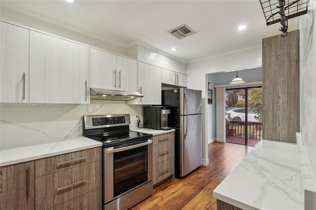 kitchen with light stone counters, stainless steel appliances, under cabinet range hood, ornamental molding, and visible vents