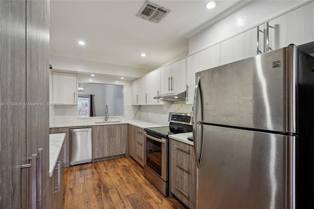 kitchen with a sink, visible vents, stainless steel appliances, light countertops, and under cabinet range hood